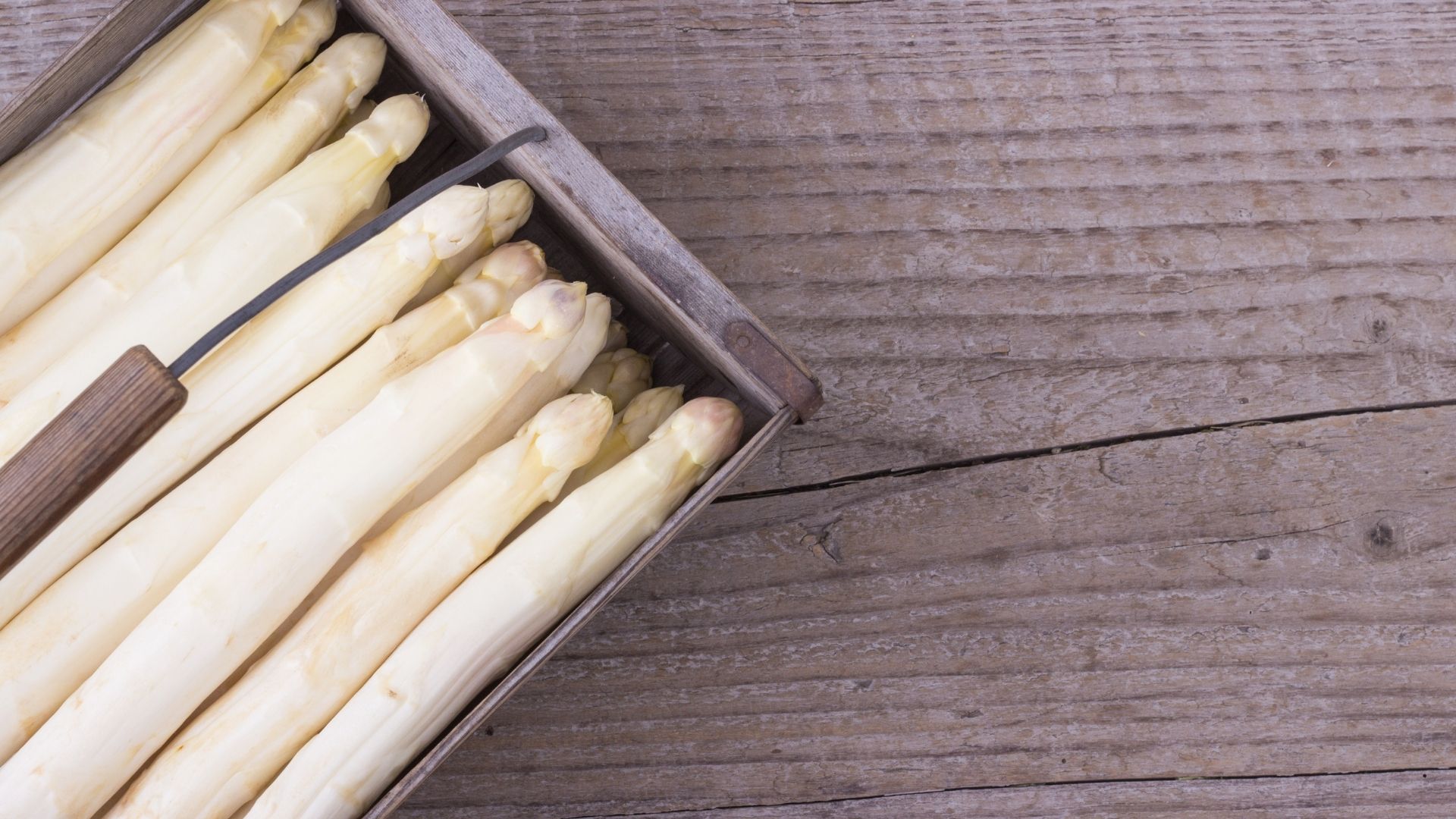 birds eyes view of white asparagus sitting in a basket on top of a wood grain table