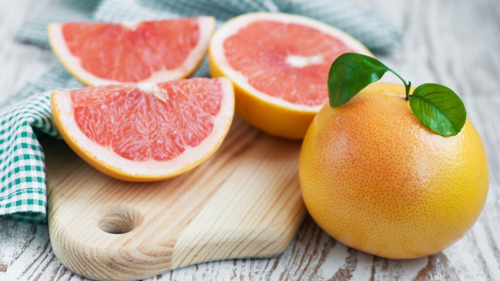 grapefruits on a cutting board table with an uncut grapefruit sitting next to them
