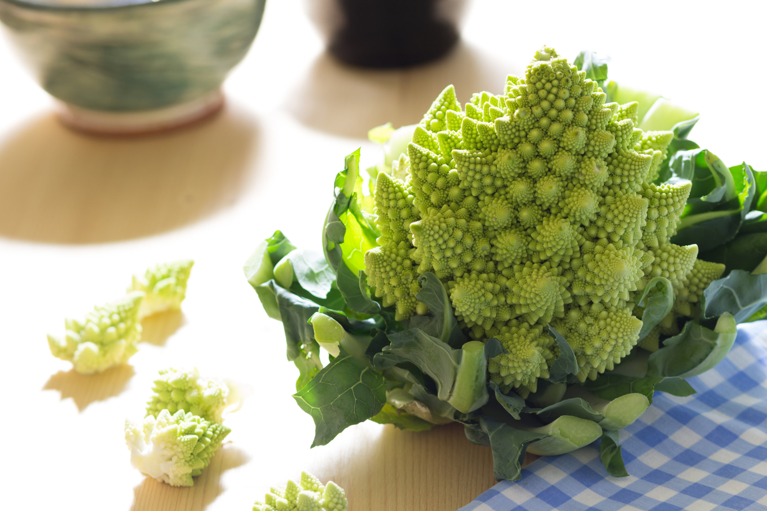 romanesco broccoli or cauliflower with florets scattered on a pale wood background and gingham cloth.