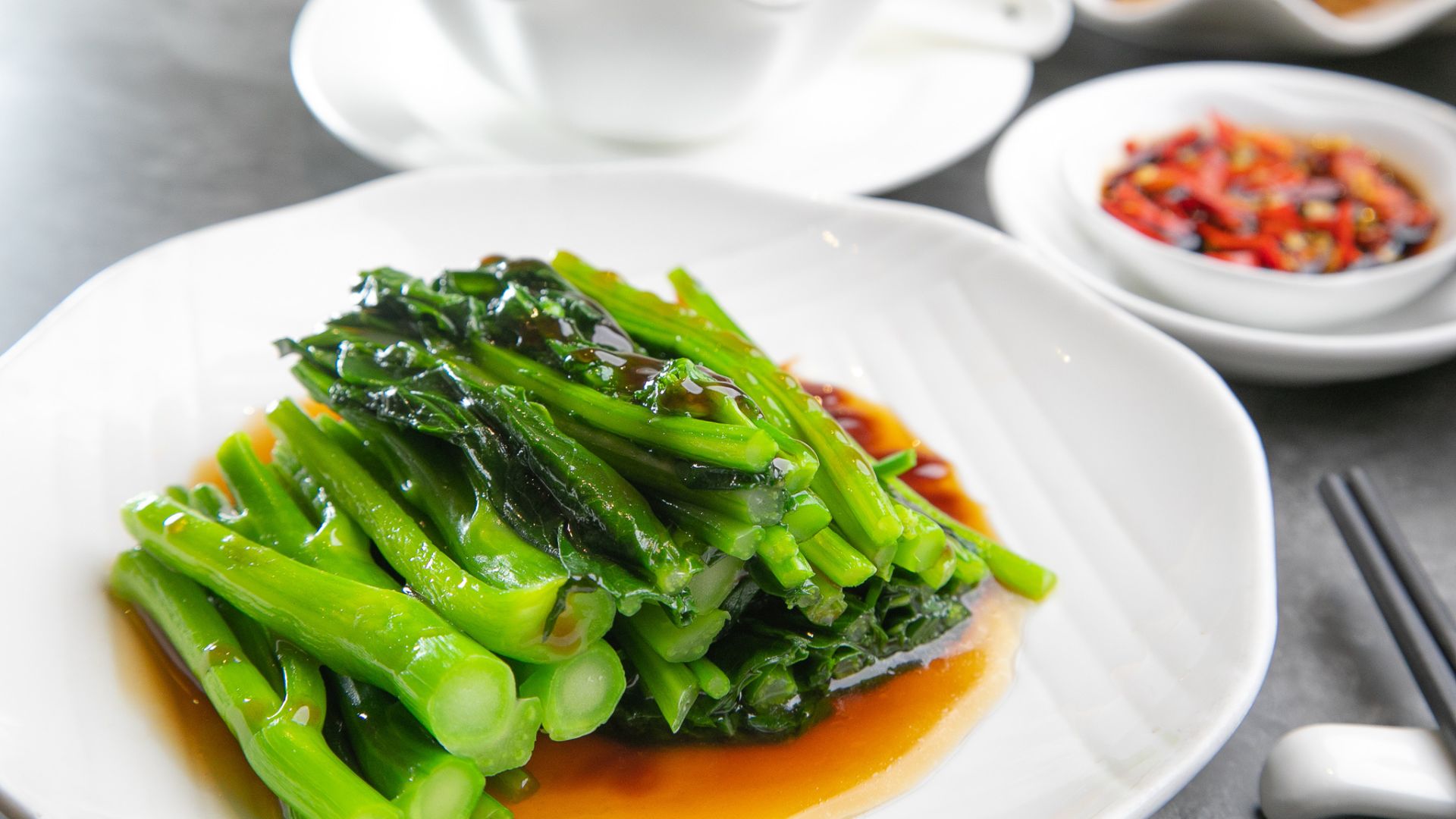 Chinese broccoli displayed on a white plate with another dish out of focus