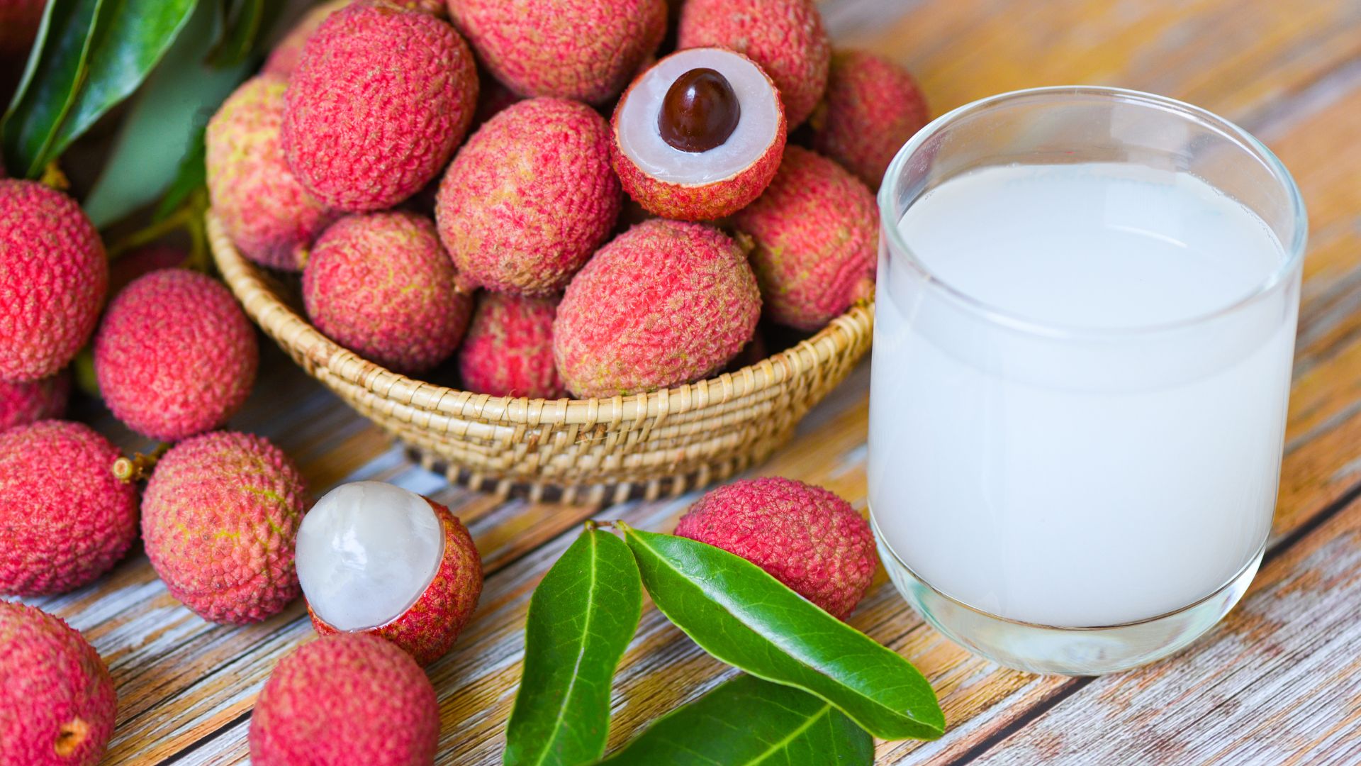 lychee fruit in a basket sitting on to of a table with a glass drink