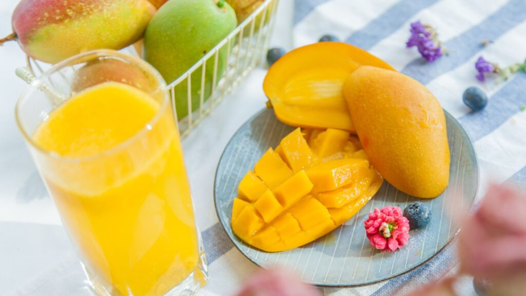 champagne mangoes sit on a plate with one cut up and the other sliced in half with a healthy drink and little berries