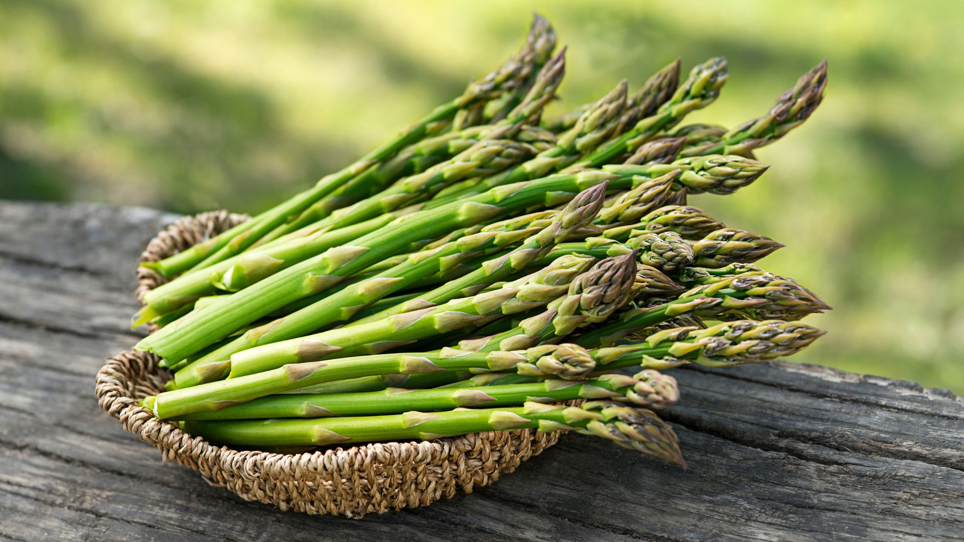 freshly cut asparagus vegetables sits in a small woven basket out in the summer weather