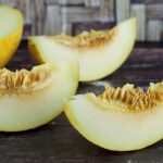four slices of galia melons on display on a dark stained table