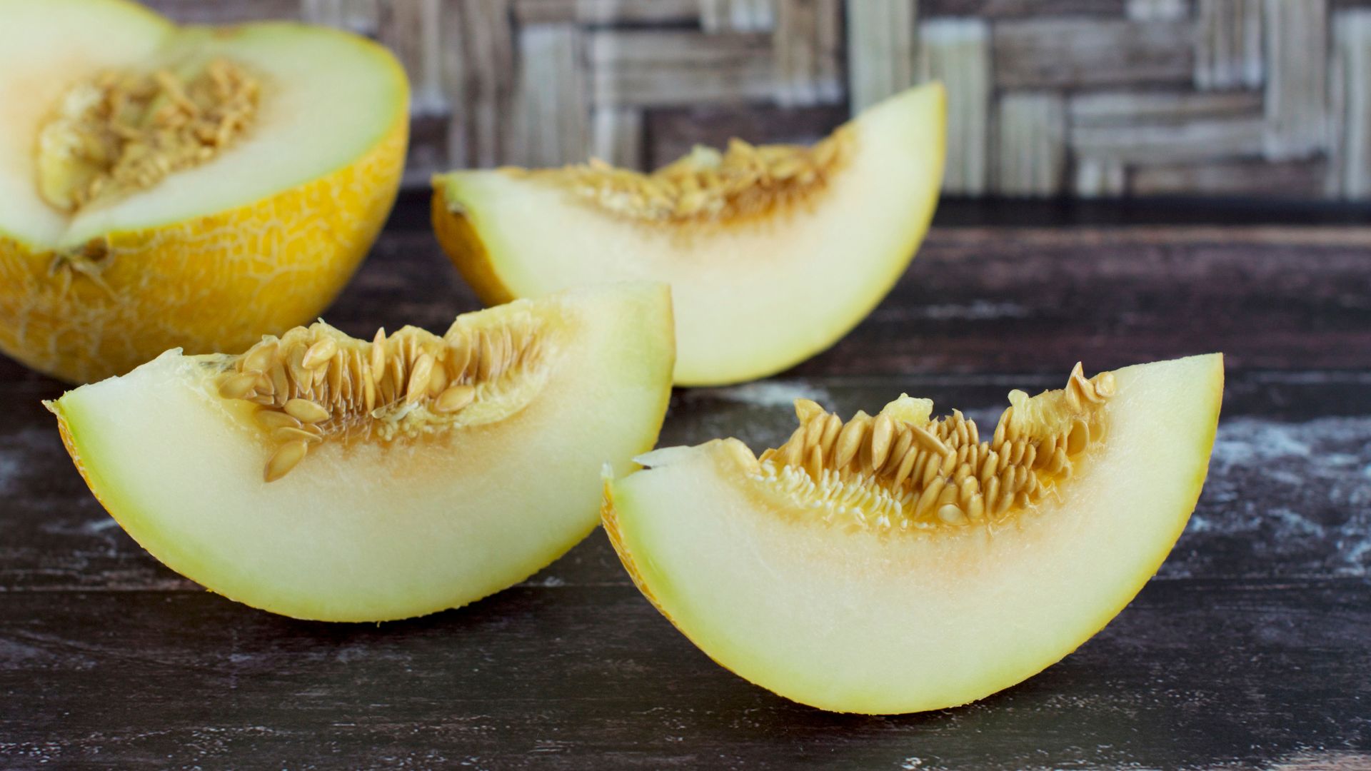 four slices of galia melons on display on a dark stained table