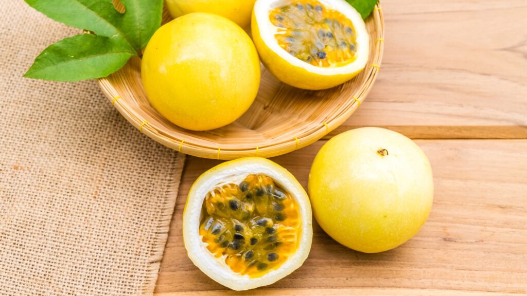 sliced passion fruit rests in a basket with some passion fruit next the basket on a wooden table