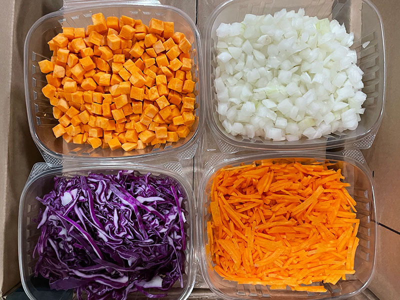 four separate plastic containers with chopped sweet potatoes, onions, purple cabbage and carrots